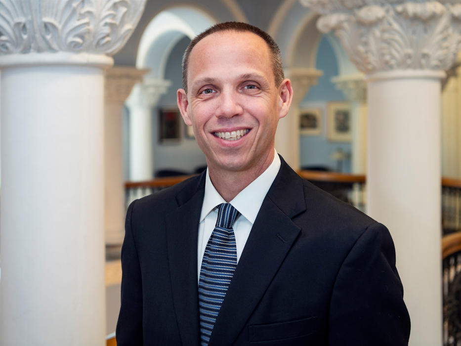 Dr. Jack Watson, wearing a suit and tie and standing in front of two large columns, smiles broadly at the camera.