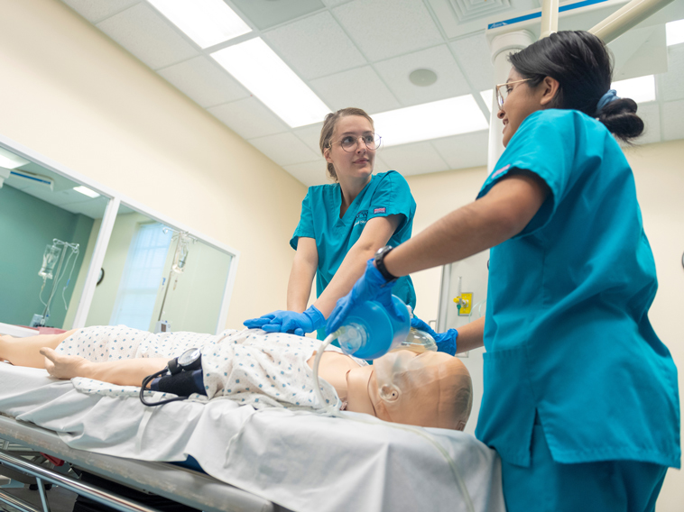 Two nursing student practice doing CPR on a manikin.