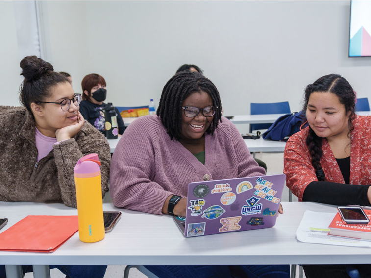 three social work students sit around a laptop while doing a project together.