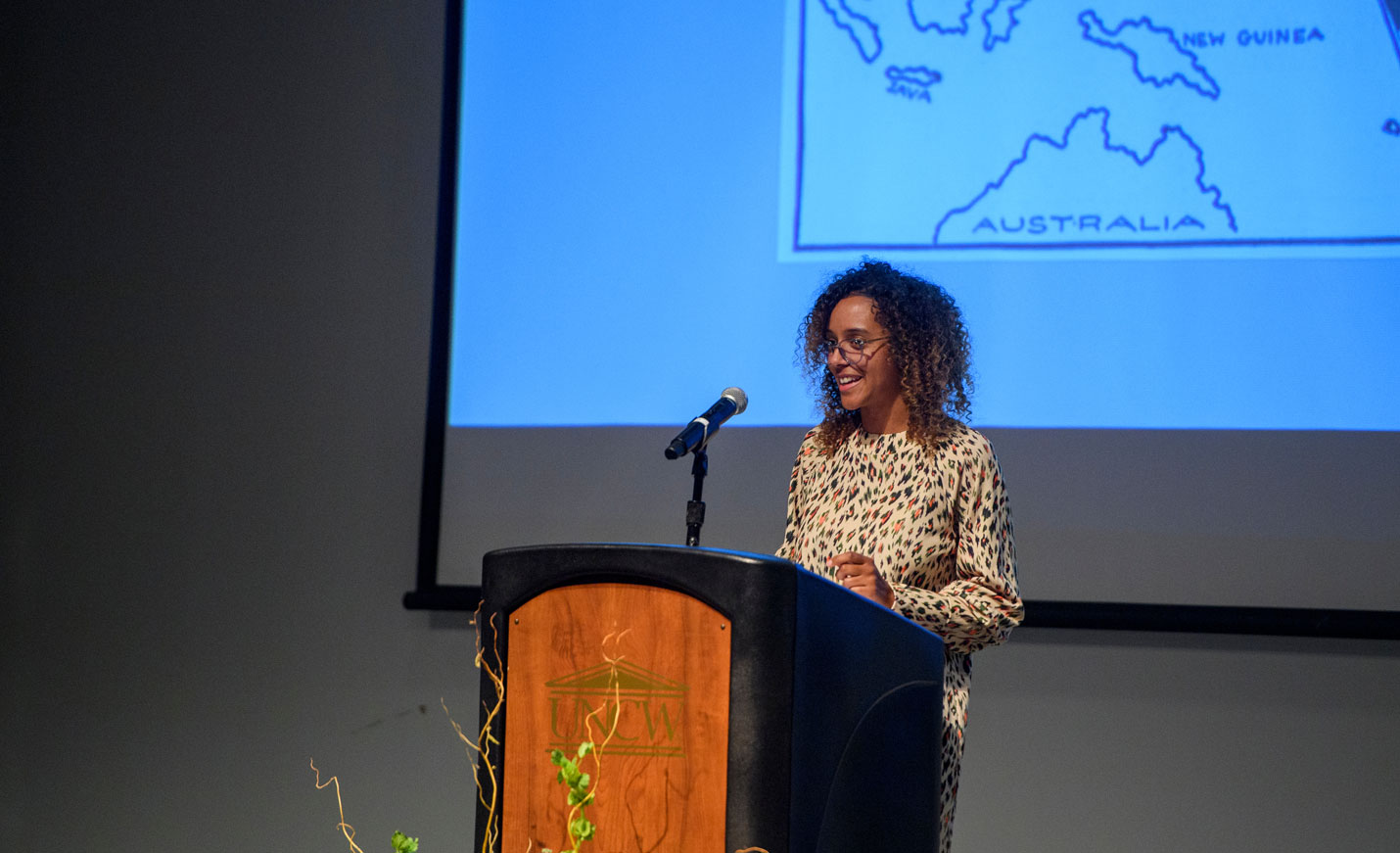 Lecturer at podium with map projected in the background 