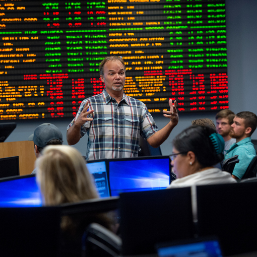 Teacher standing in front of a stock tickboard while giving a lecture