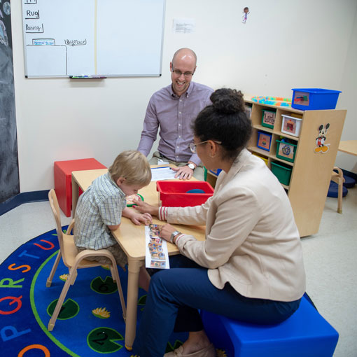 Two adults showing a book to a kid at a table.