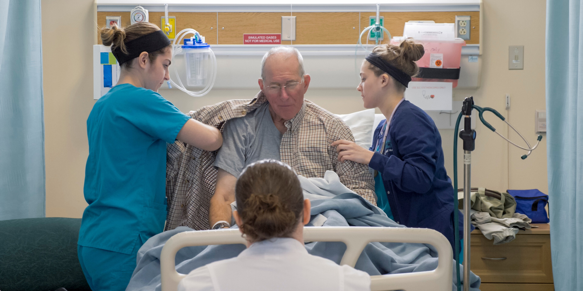 two nursing students help an older patient get dressed