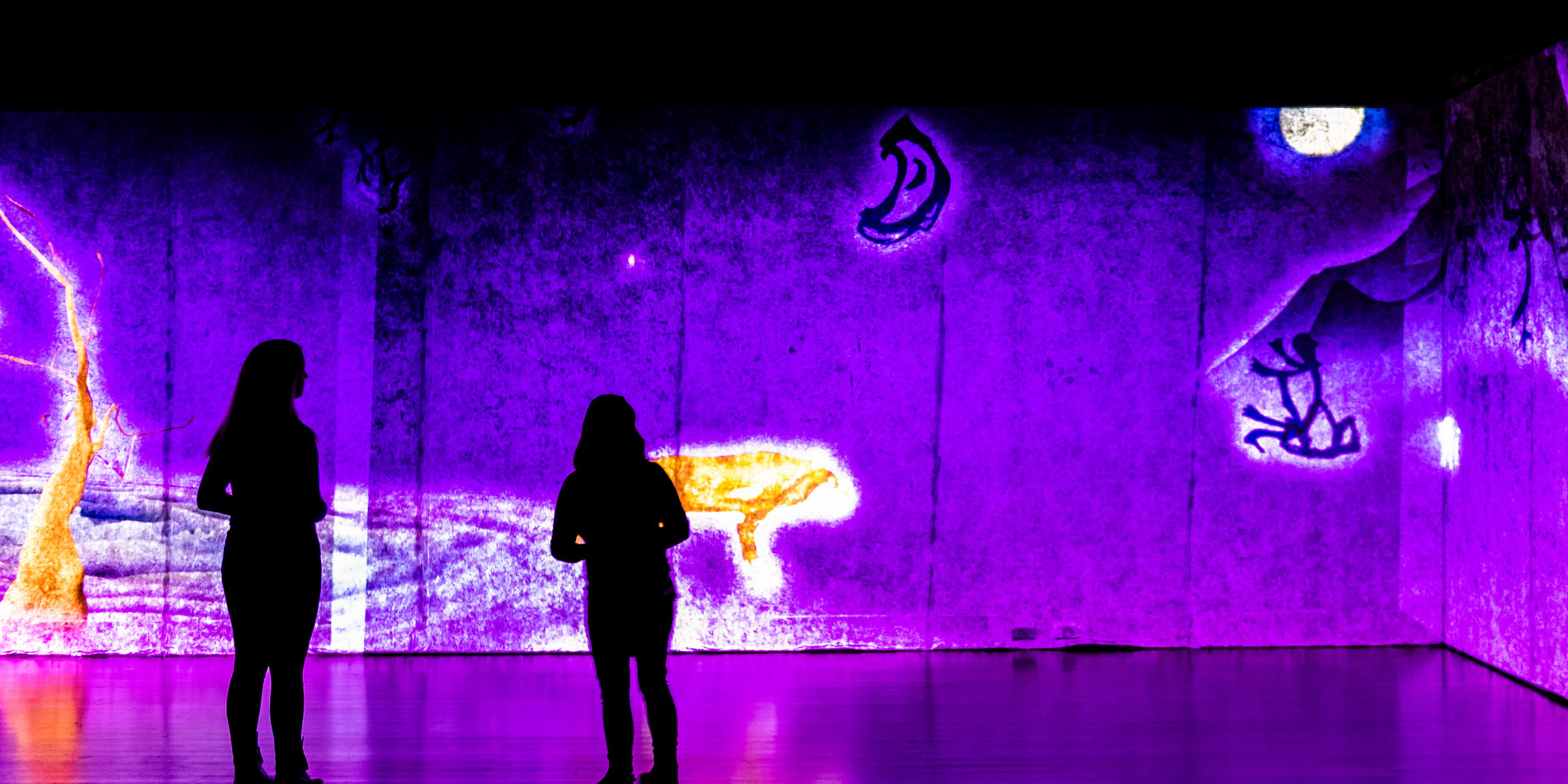 Two people stand in a dark room and admire projects made by Digital Arts students