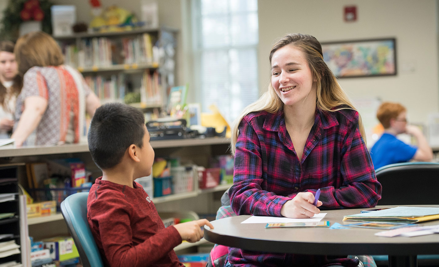 A UNCW student works with a young boy in a teaching lab; both are seated at a table