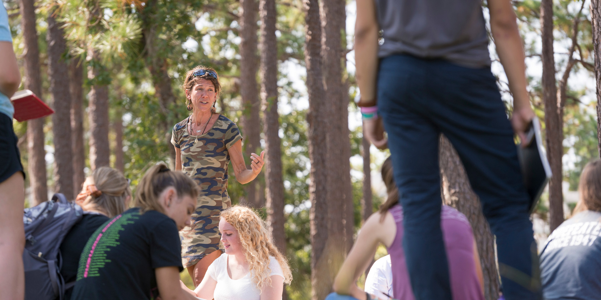 A group of students listen to a professor speak during an outdoor class