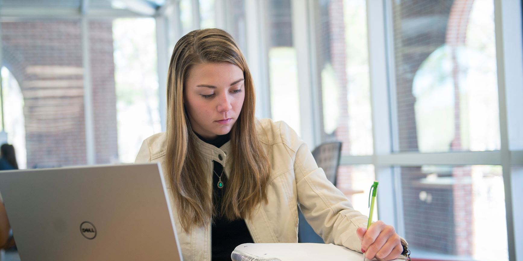 A student works on a laptop in the library while taking notes 