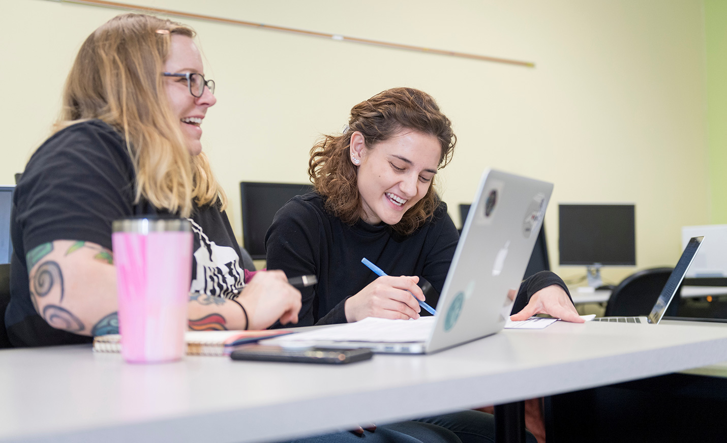 two smiling students working at a laptop
