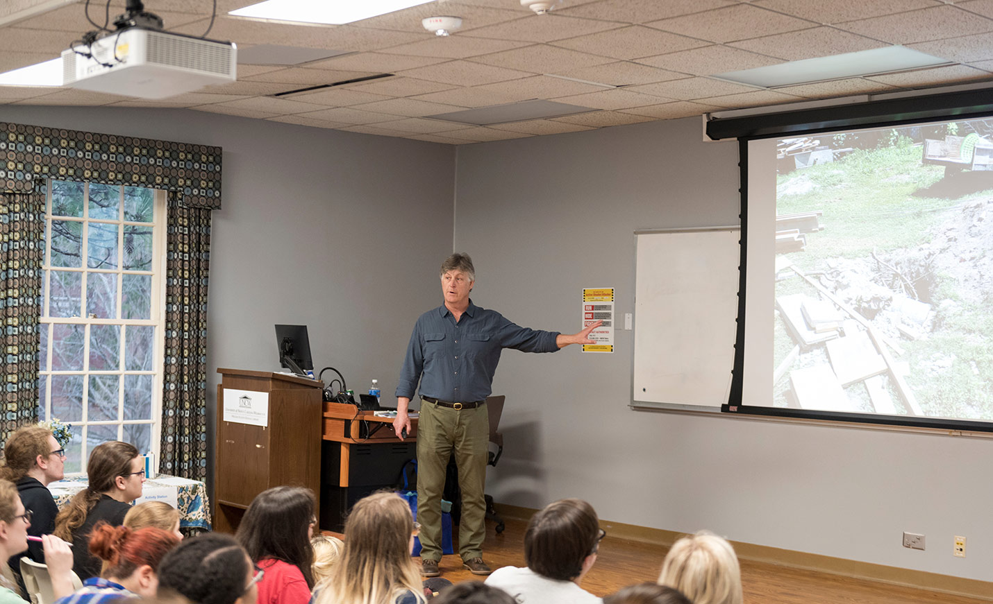 faculty members lectures to class and points at image on screen