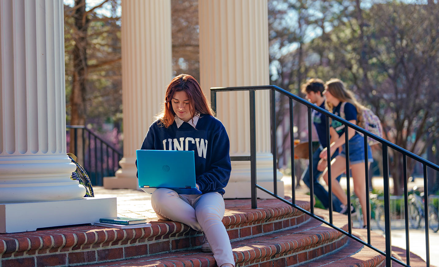 student working on a laptop outdoors on the stairs of UNCW Library