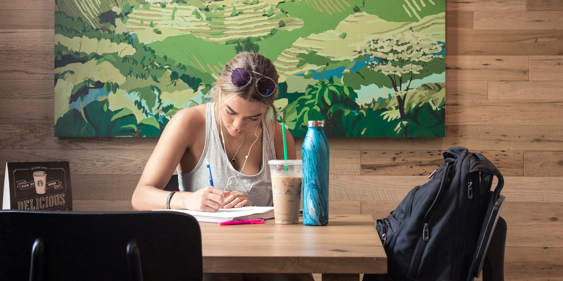 A student works in a notebook while sitting at a table in The Hub