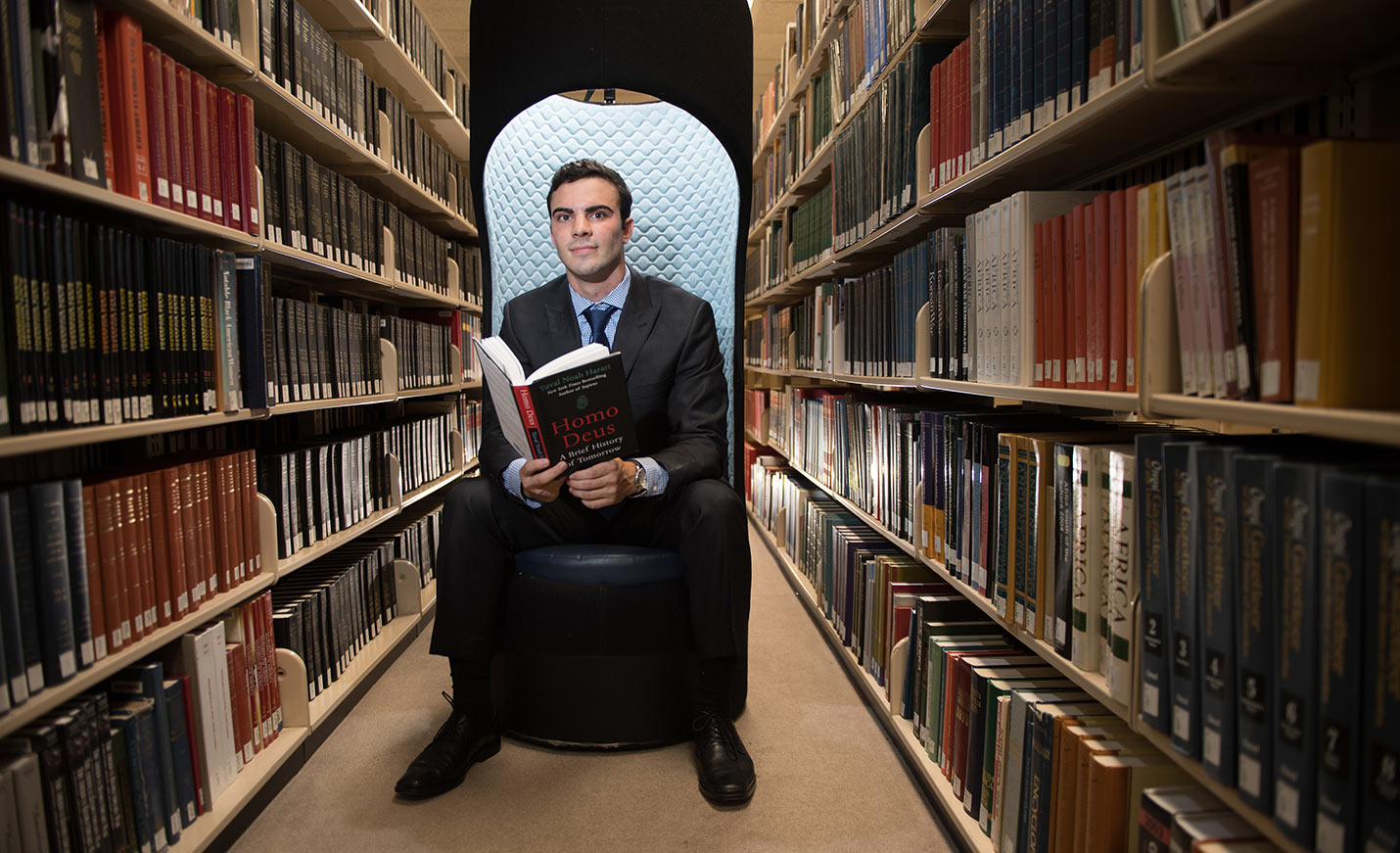 UNCW student sitting in a chair in the stacks in UNCW Library.