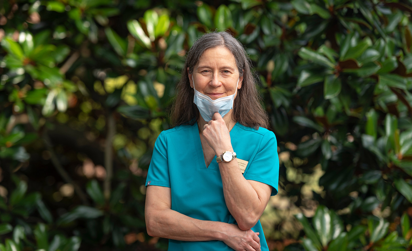 A woman in teal scrubs with a mask pulled down over her chin