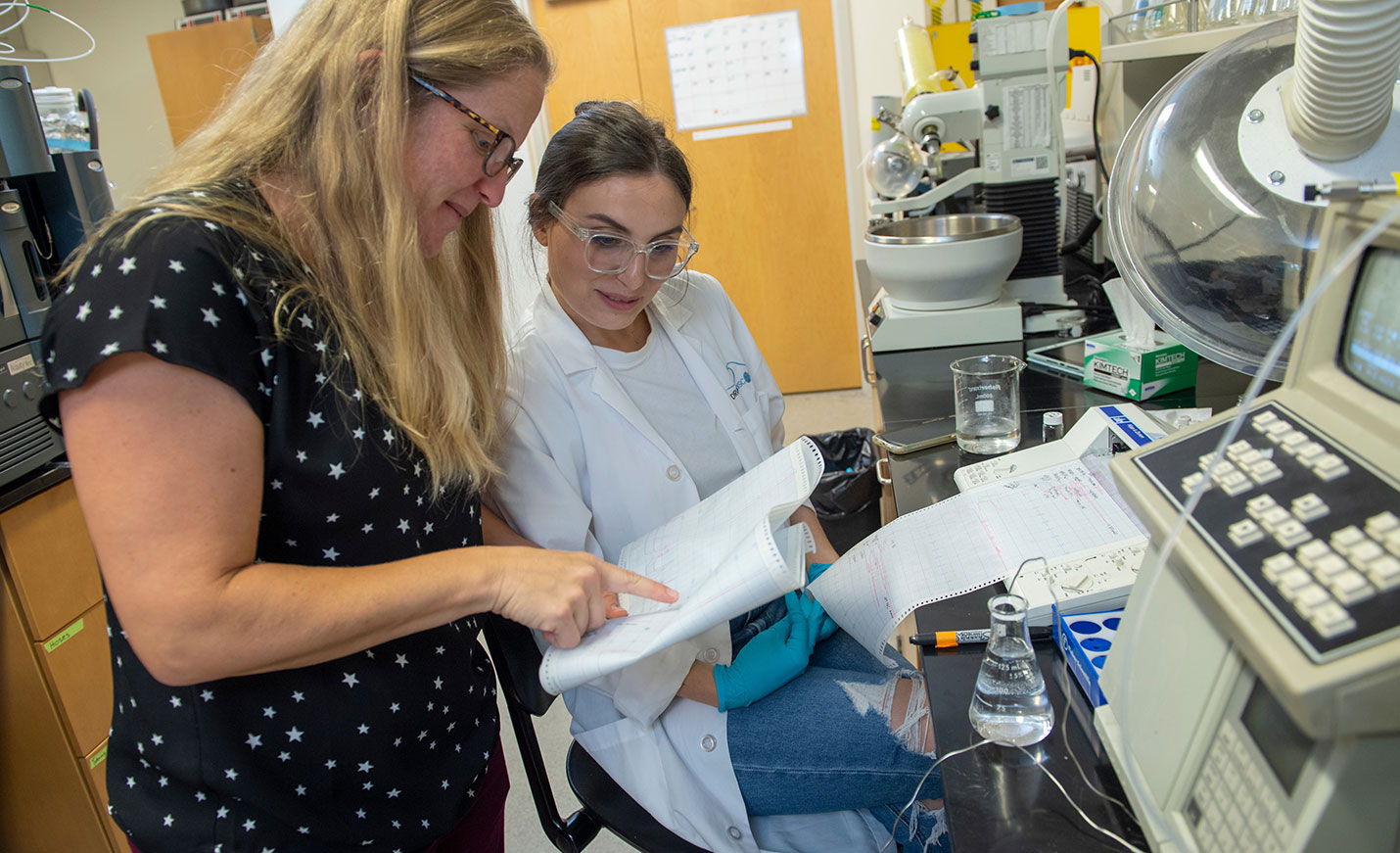 A woman looks at a printout of medical results while another woman holds the paper