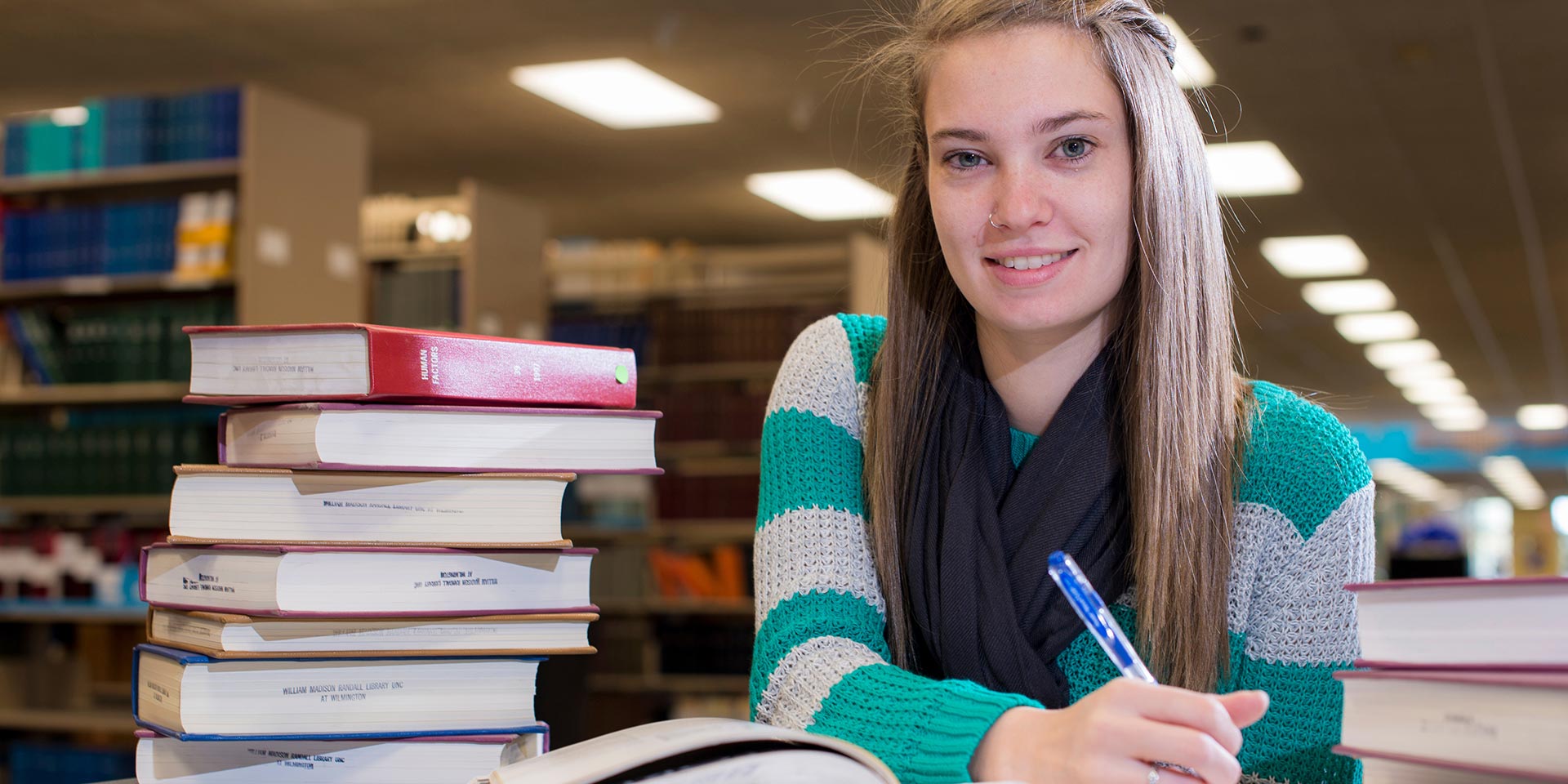 A student smiles for the camera as she writes in a book