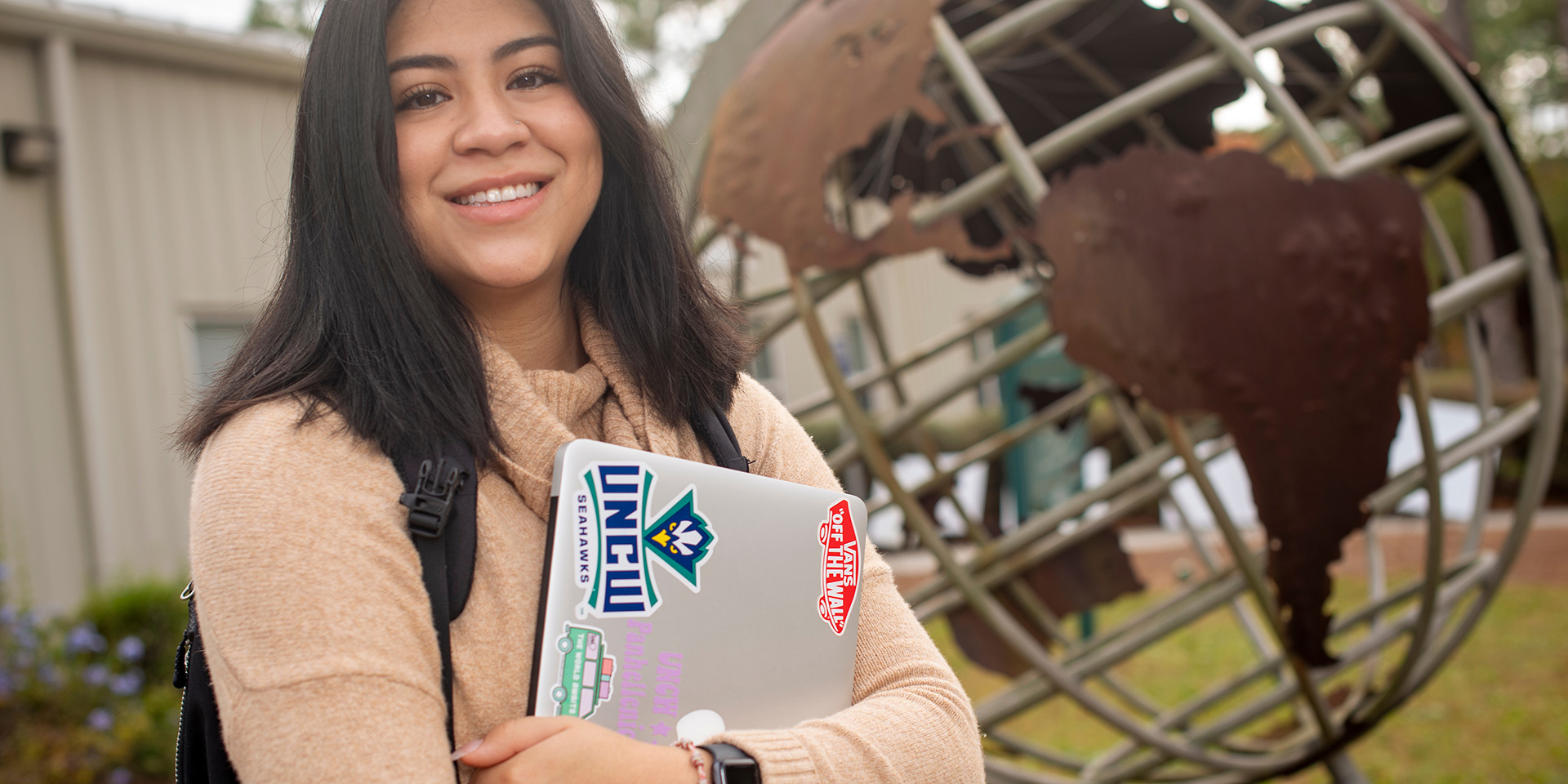 A student standing in front of the globe statue on UNCW’s campus