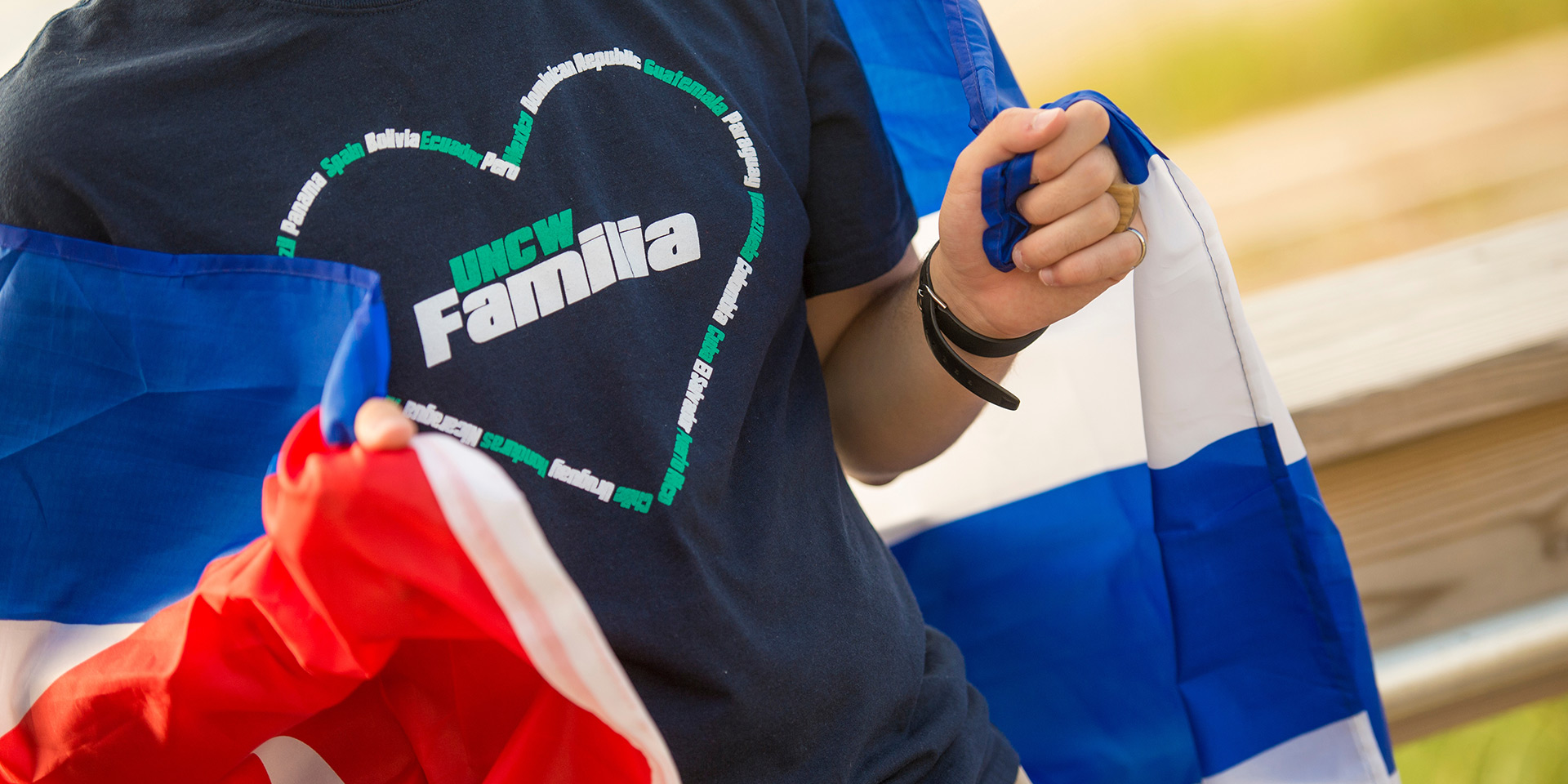 a person wearing a shirt that reads UNCW Familia inside of a heart made of indistinguishable words