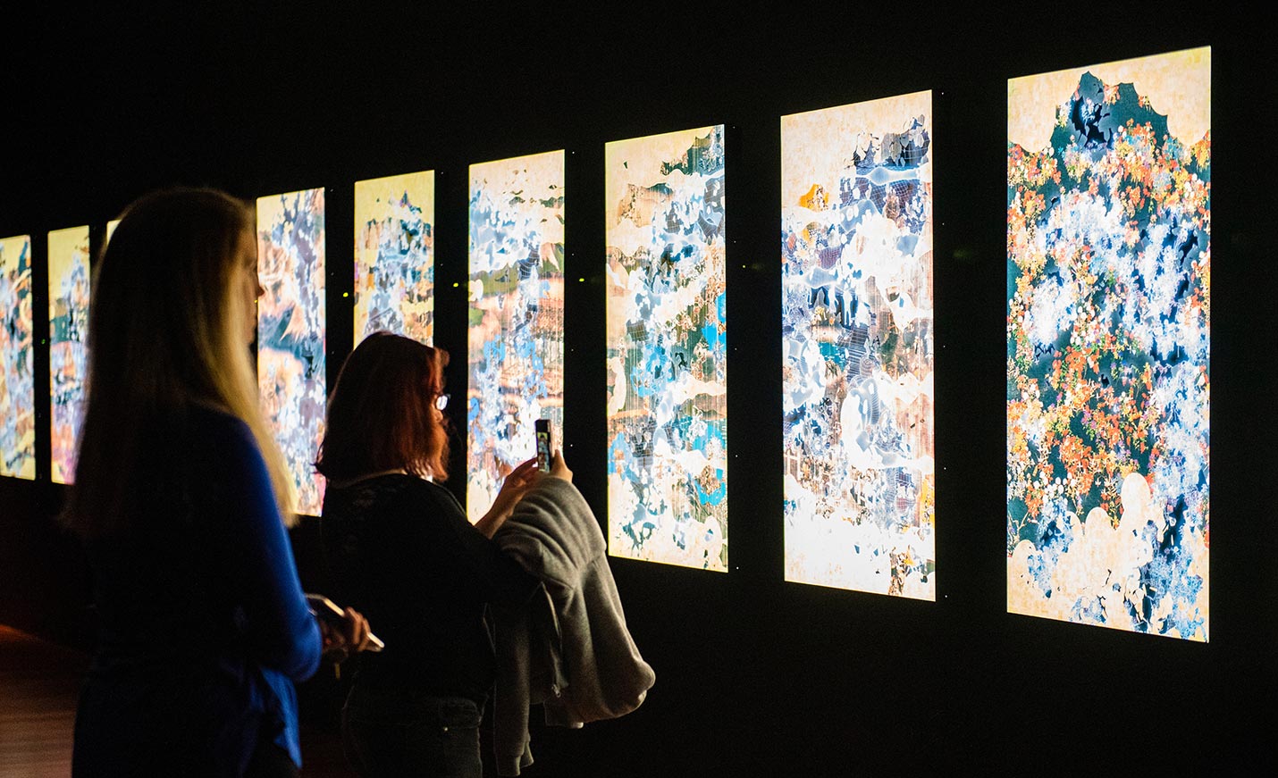 Students view an interactive art exhibit; one student takes a photo with her phone