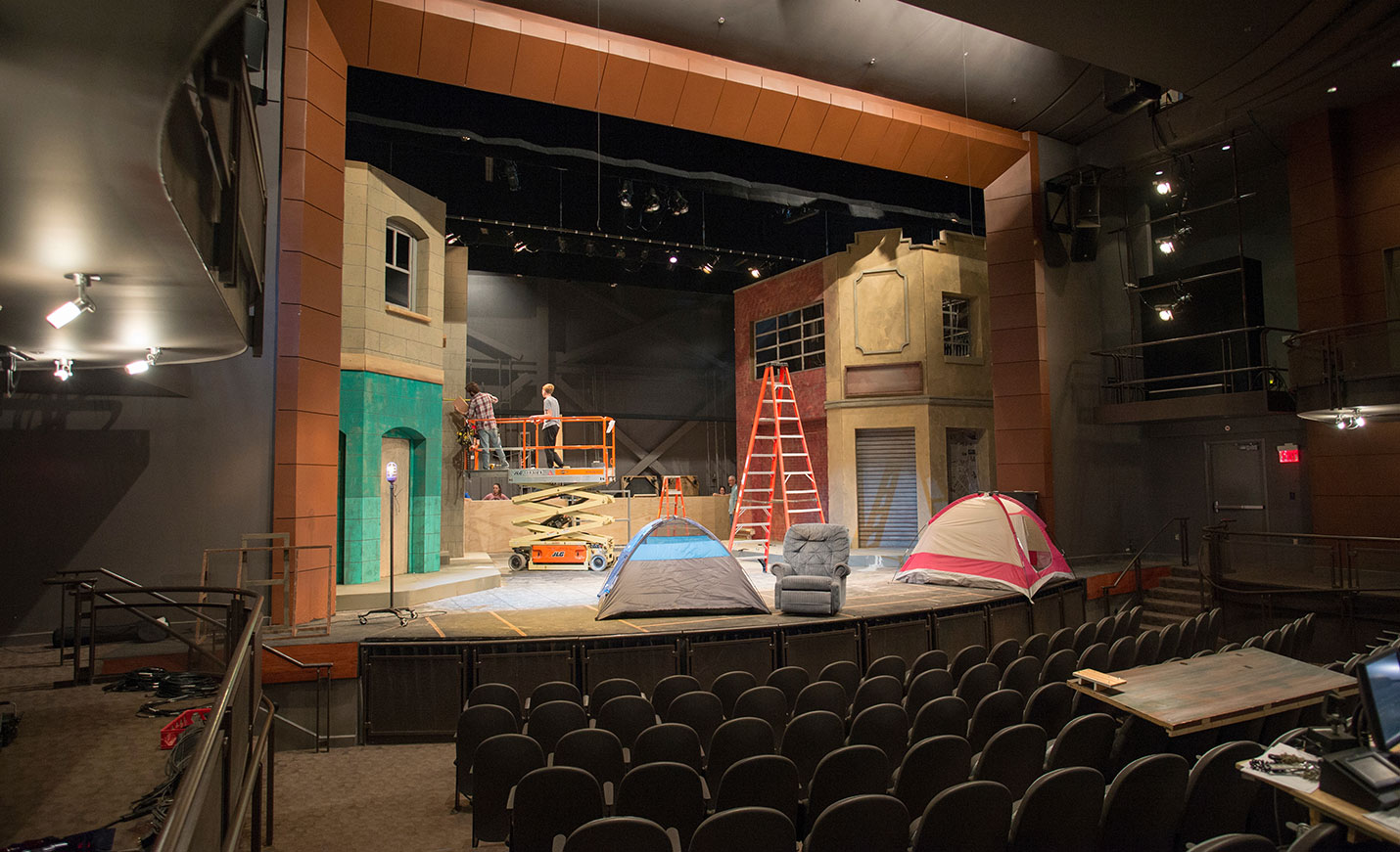 Two tents, a ladder and a mobile scaffold with a man standing on it on a theater stage
