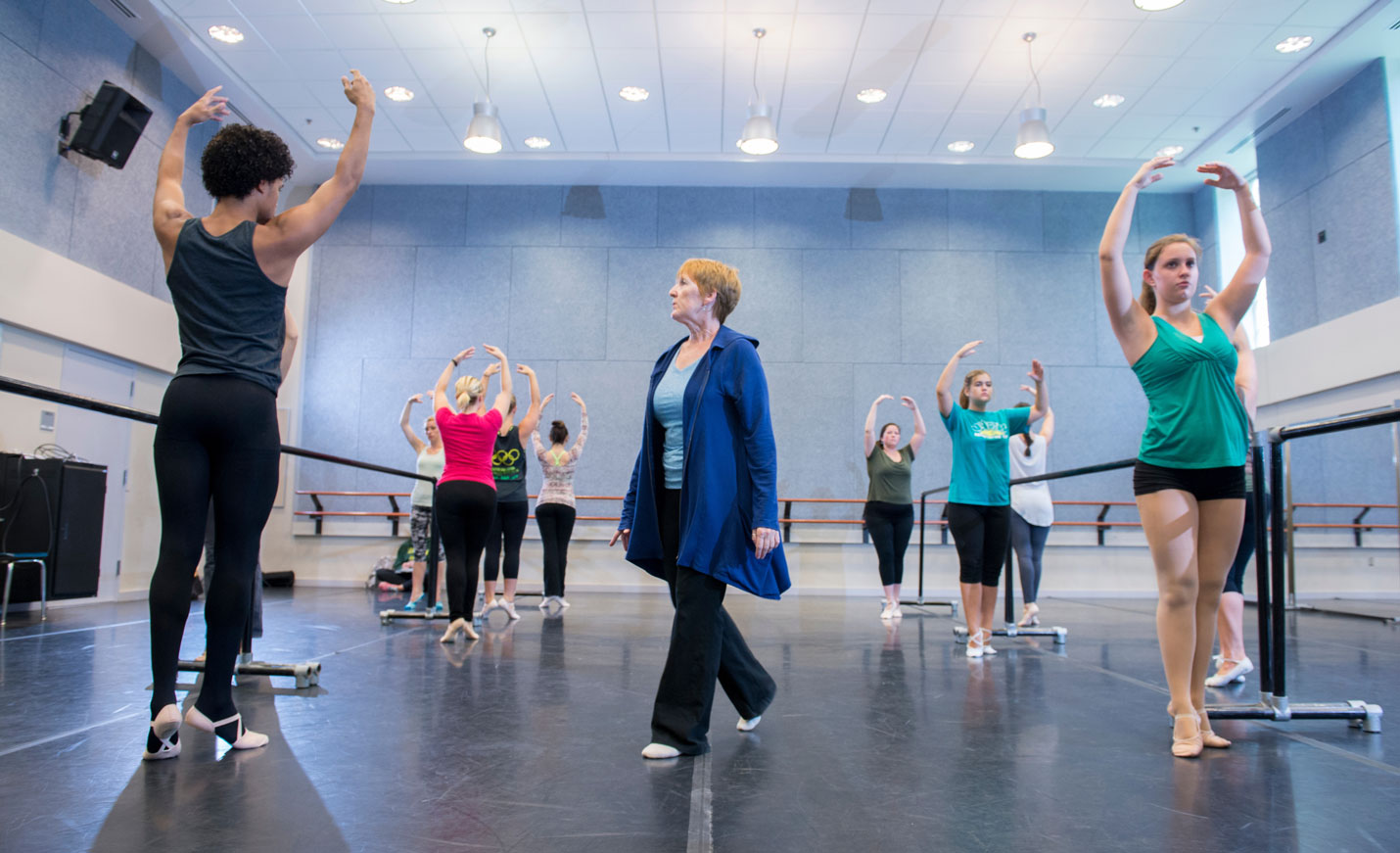 An instructor watching students in a ballet class with arms raised above their heads