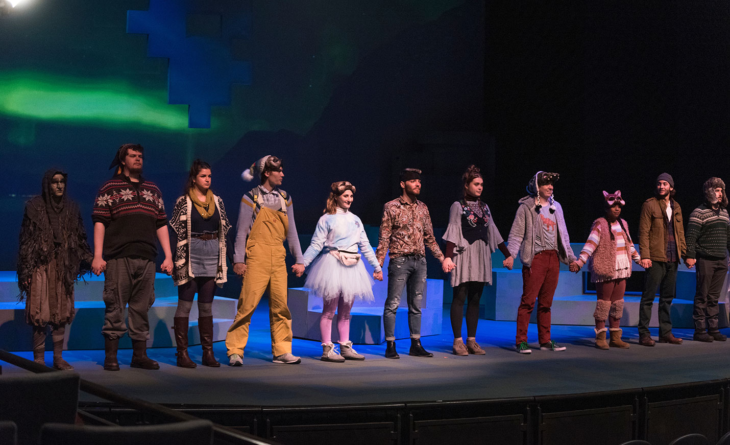The cast of a play holding hands and preparing for a bow at the end of a play