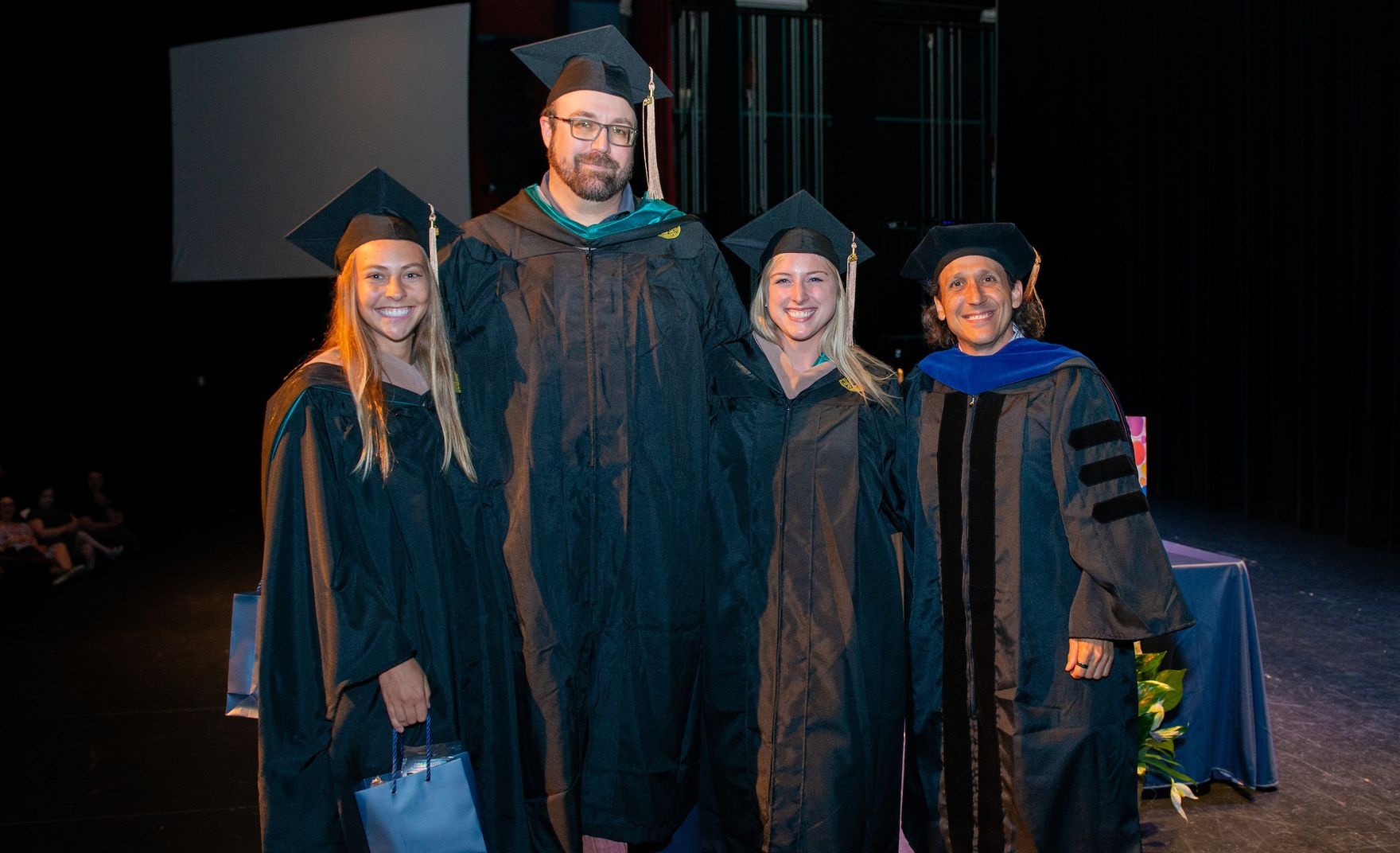 CSB MSAC graduates pose together on the stage for commencement. 
