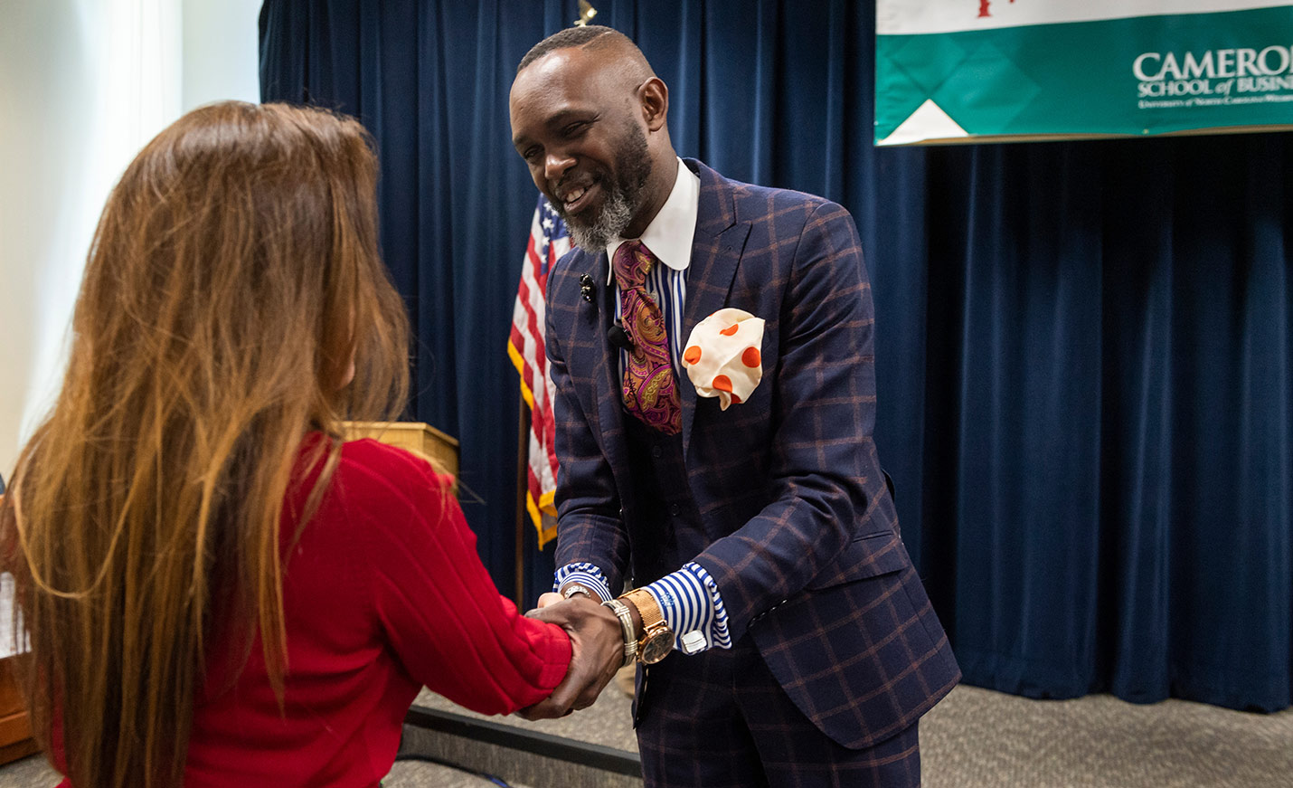 A faculty member shakes hands with a student in front of a stage curtain