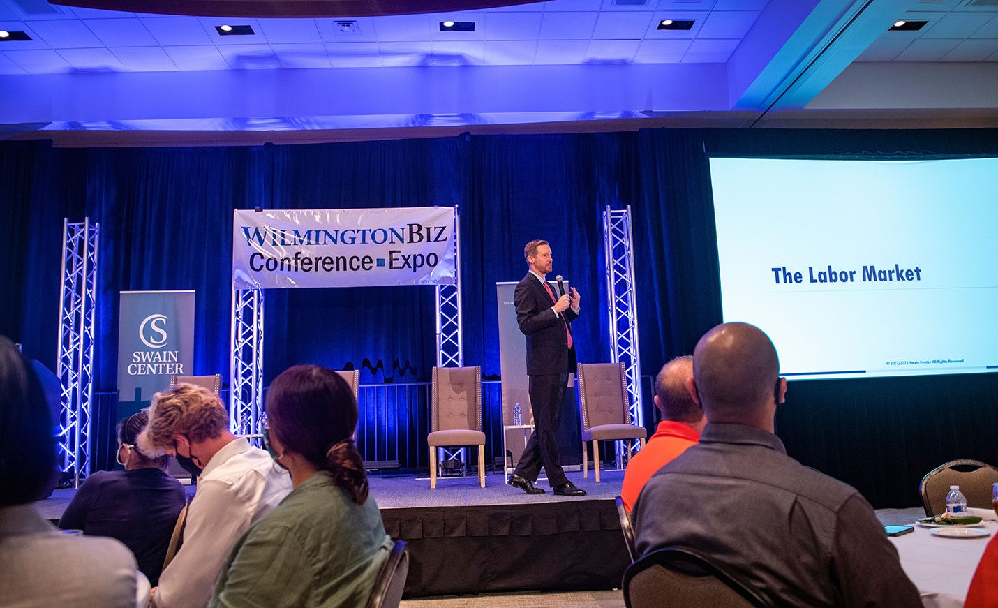 A speaker with a mic onstage at a business conference