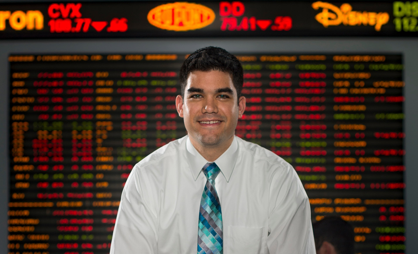 Associate Professor Daniel Soques in front of the stocks ticker in Congdon Hall