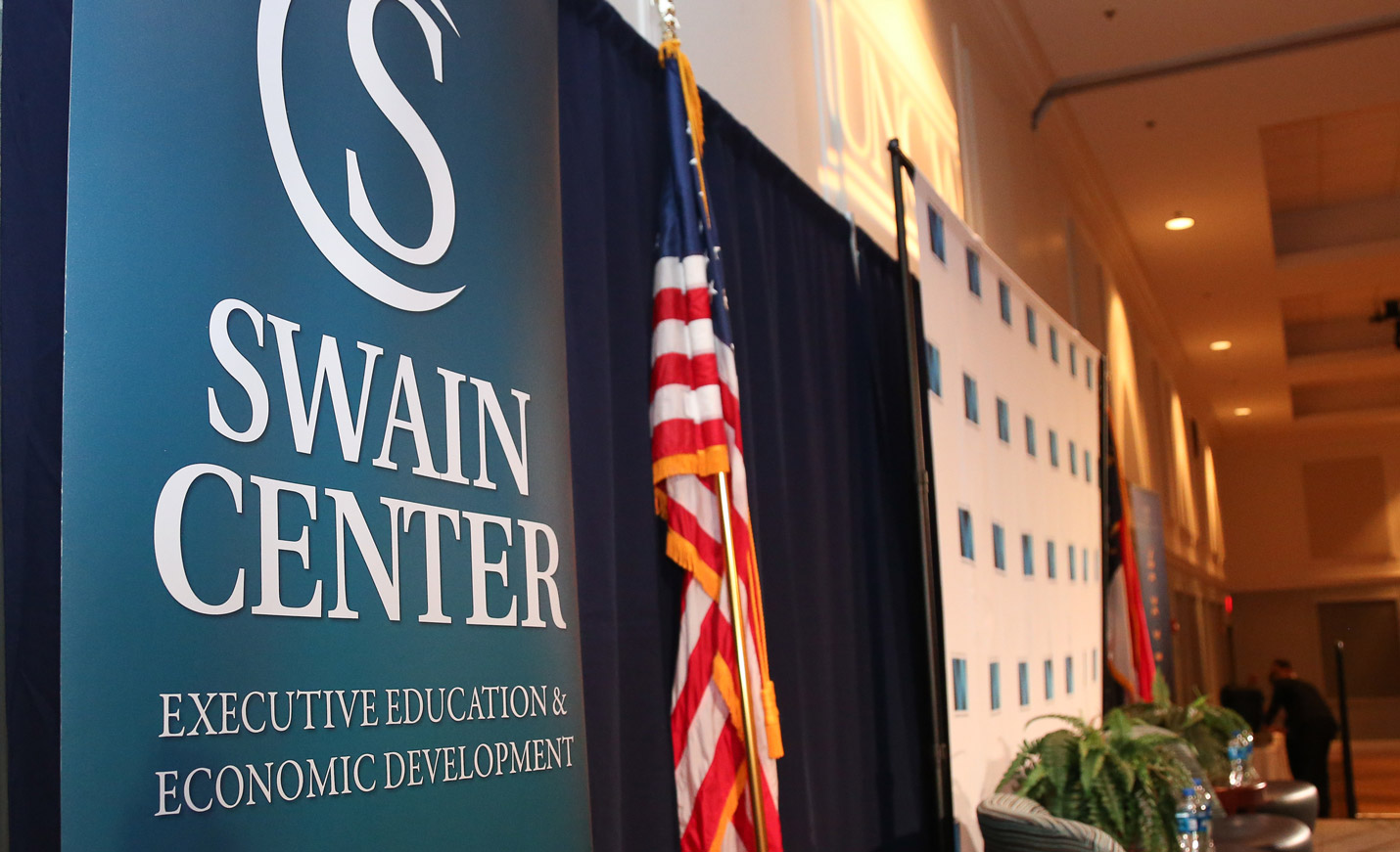 A side view of the stage and a Swain Center for Executive Development sign; the stage also displays the American and North Carolina flags 