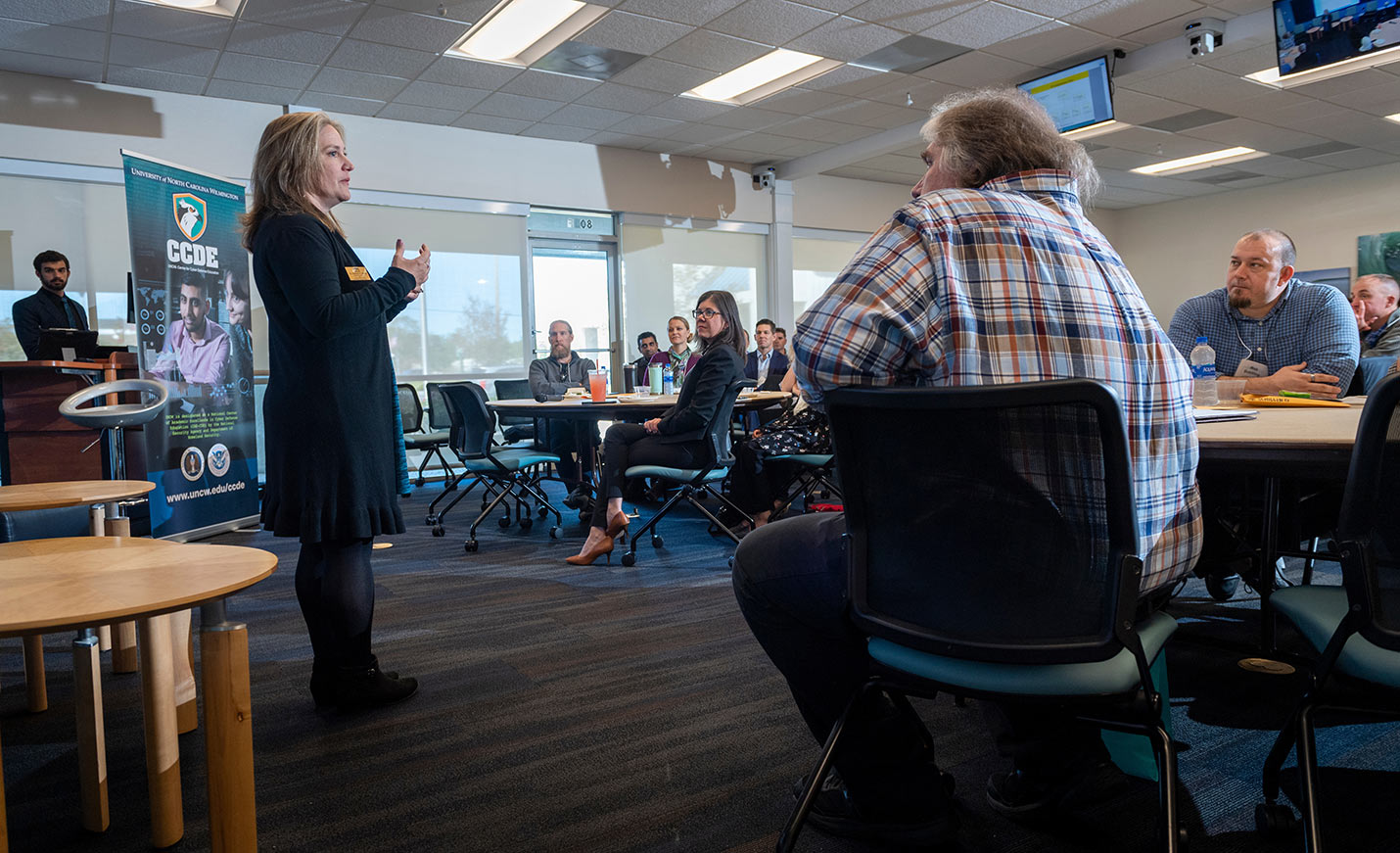 A speaker talks during an event to an audience seated at tables