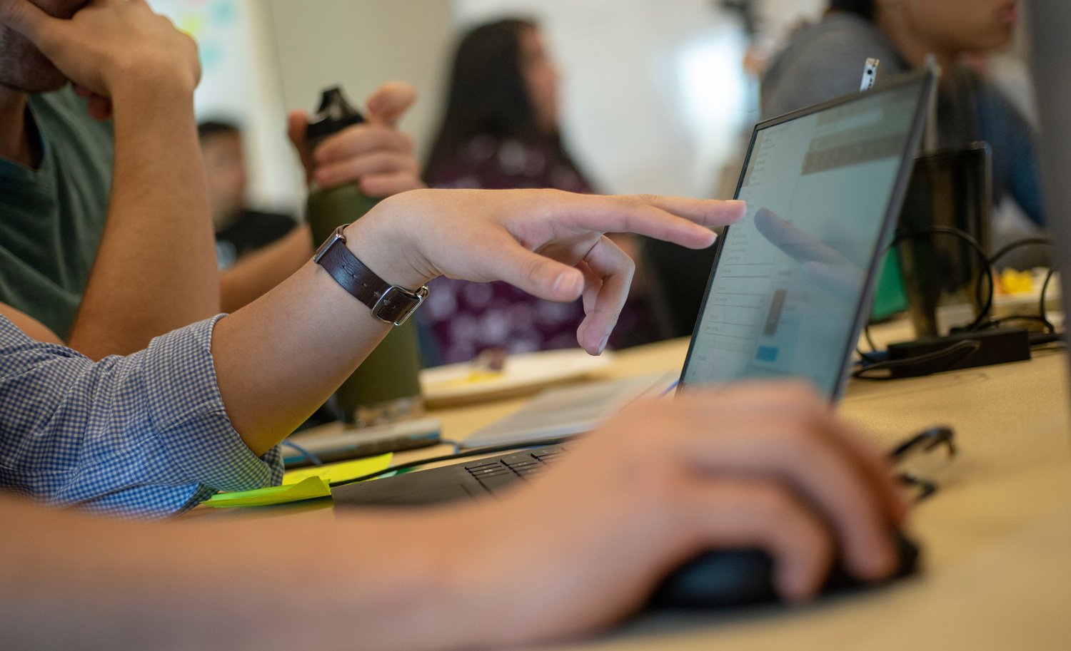A student working on a laptop, pointing to the screen to point out something to a classmate