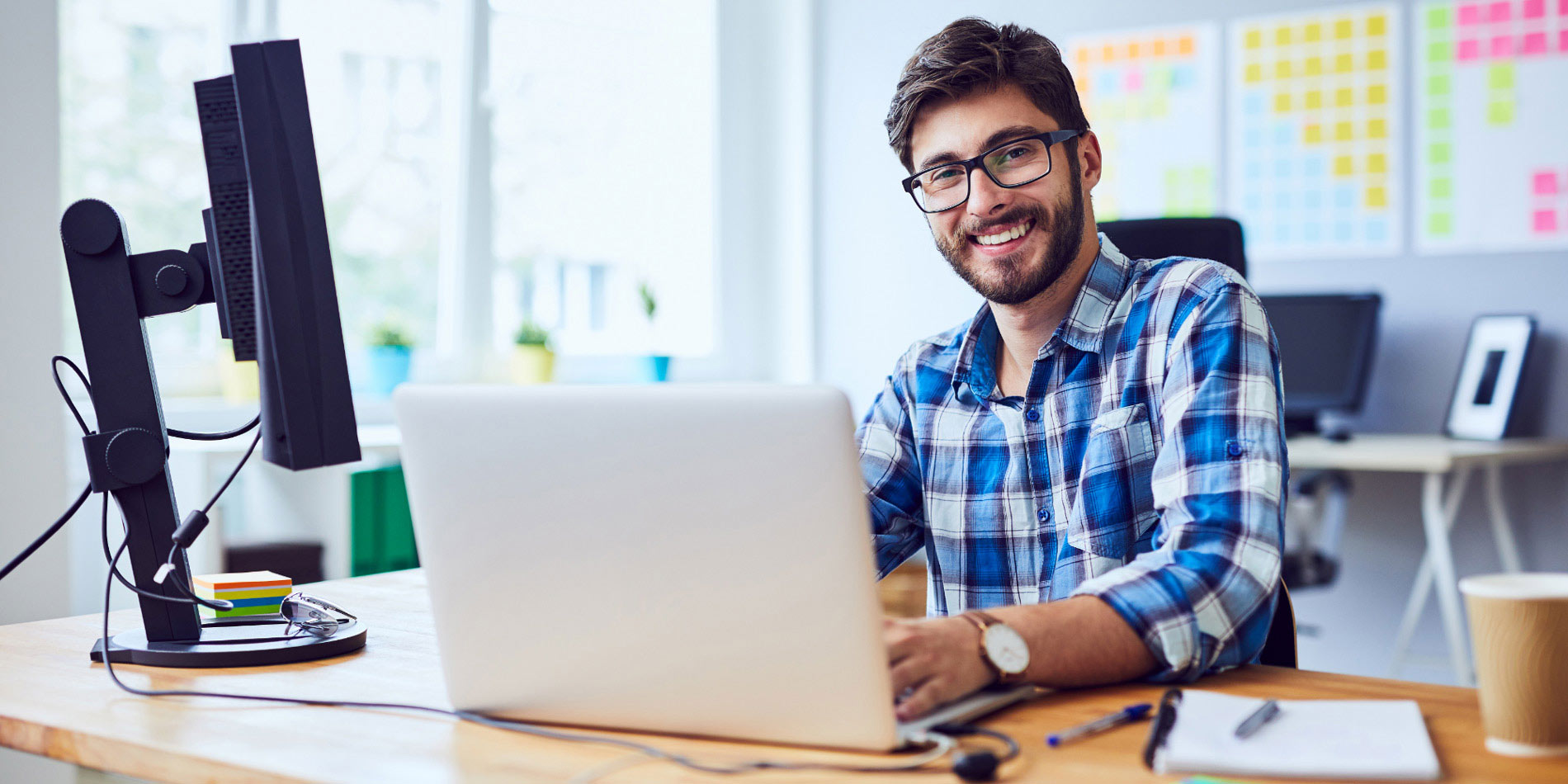 Man in plaid shirt at a desk with a laptop