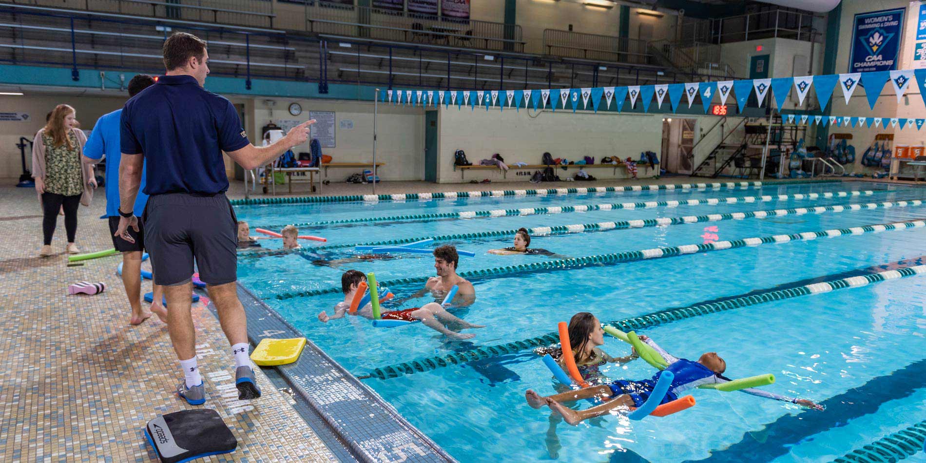 Elementary students in an indoor pool floating on pool noodles