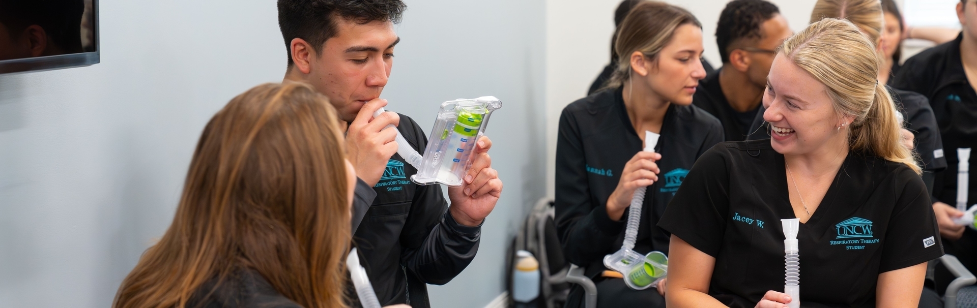 A respiratory therapy student uses a incentive spirometer while his peers watch on