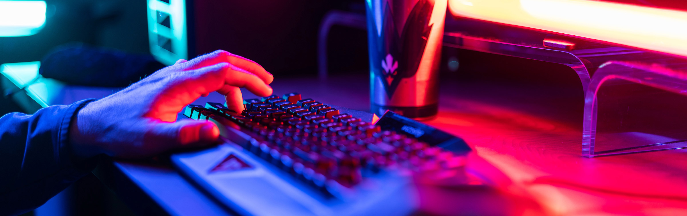 Person using a keyboard and mouse with the UNCW logo in the background and red computer light shining on the devices.