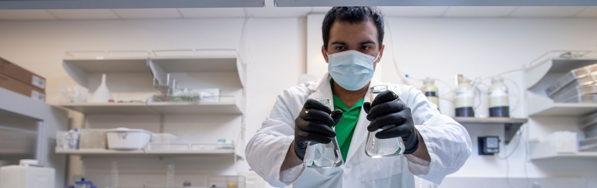  A student in a mask examines two beakers 