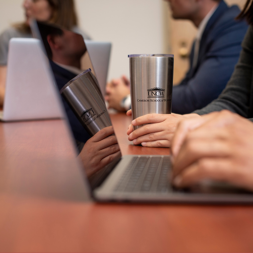 students seated at a conference table while a professor shakes a student’s hand