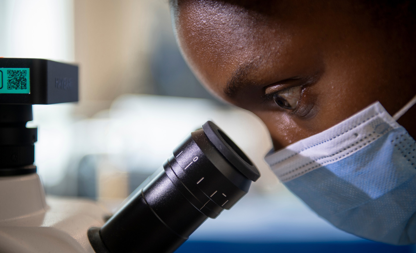 person looking through a microscope with mask on