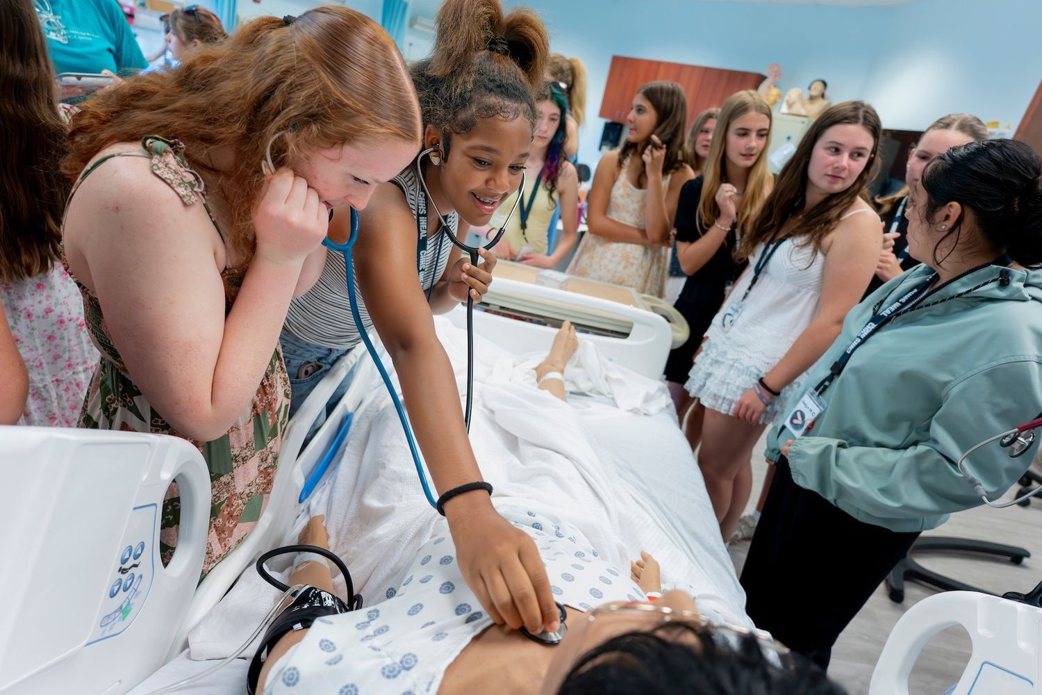 Two iHEAL summer campers listen to the heart of a manikin with a stethoscope while touring various healthcare simulation labs on the UNCW campus. 