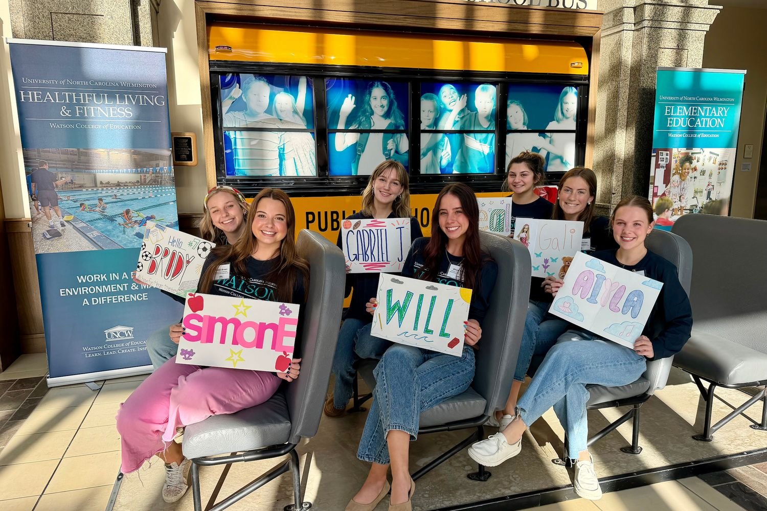 Students hold signs while sitting on the bus display
