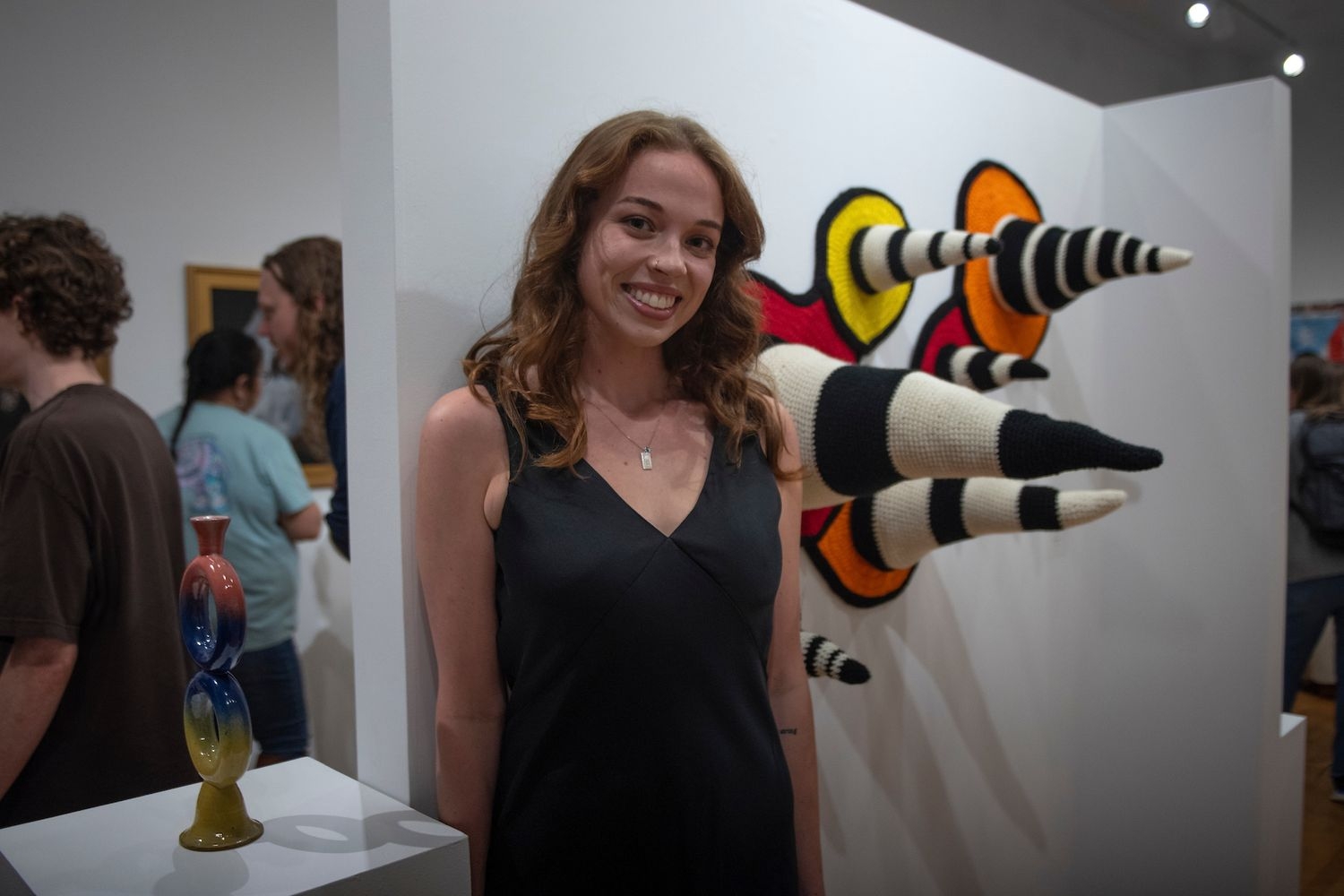 Student stands with their art piece in a gallery