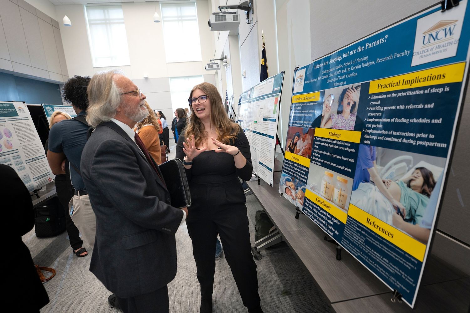 A student in business attire presents a research poster to a man in a suit.