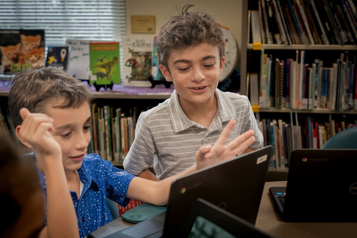 Two kids laughing while working on their laptops
