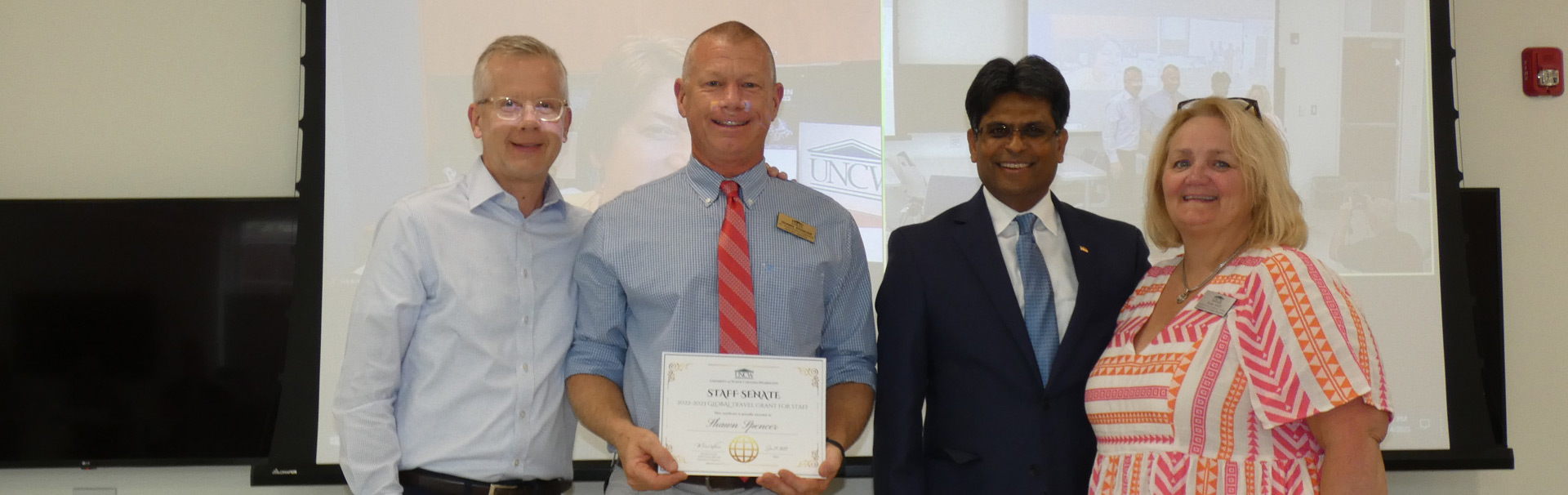 3 people standing smiling with grant award with Chancellor Volety