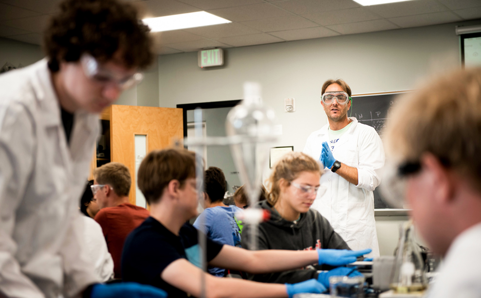 students learning in a classroom with goggles and gloves.