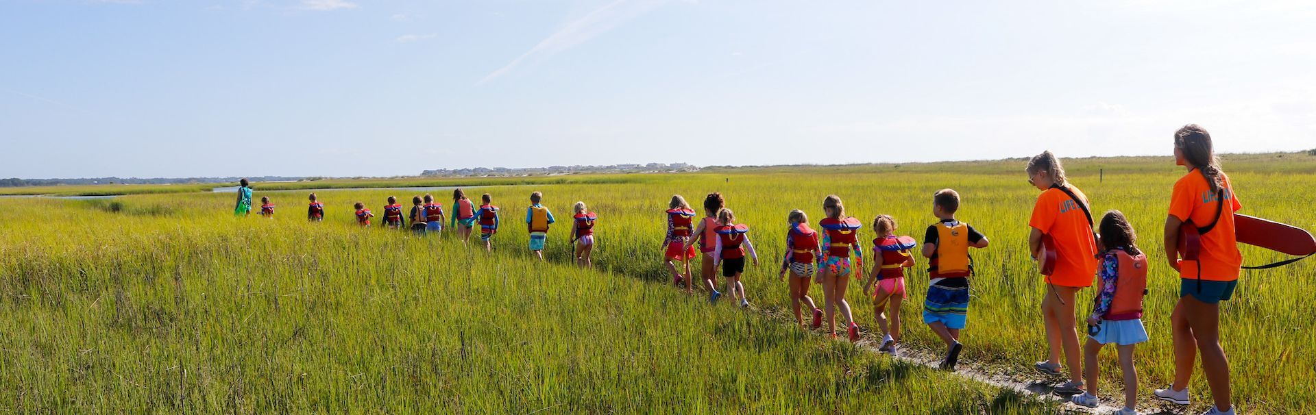 Children with life jackets walking in line through marshes with lifeguards