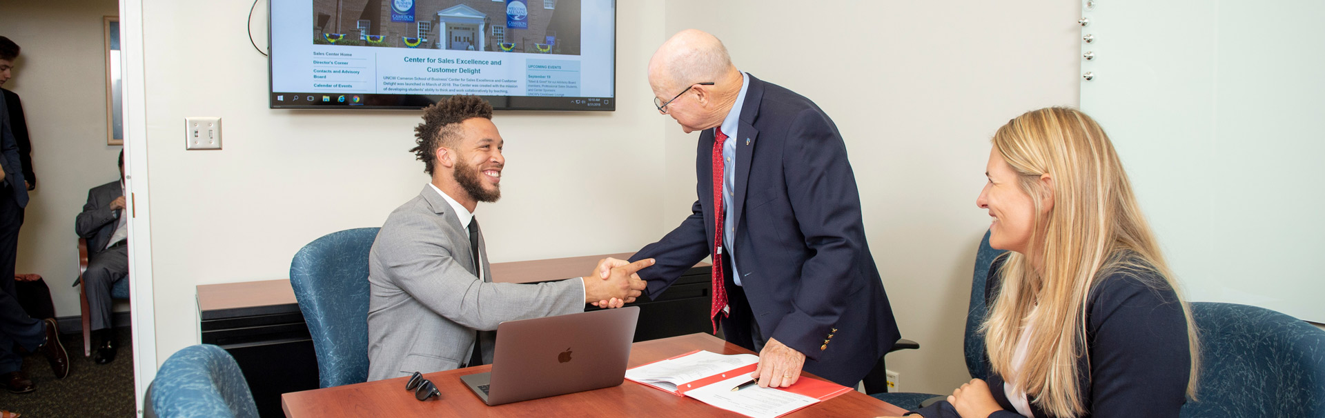 One student shakes hands with an older gentleman while the other looks on